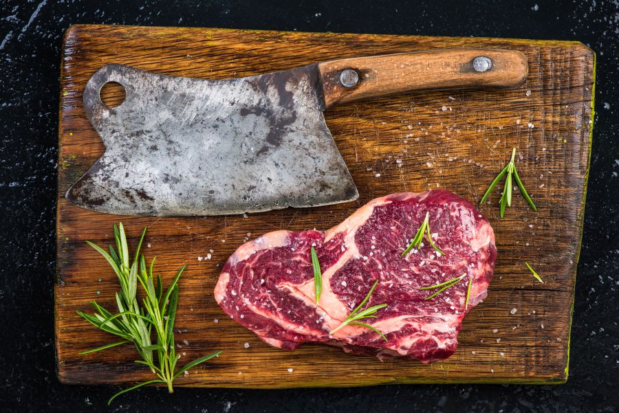 Fleischerbeil und ein Stück Steak auf einem rustikalem Holzbrett